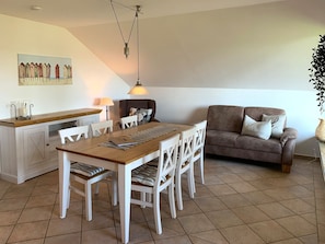 A dining area with a wooden table and white chairs, a sofa, and a painting on the wall.