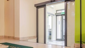 A hotel lobby with a green carpet, a reception desk, and a glass door leading to another area.