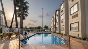 A swimming pool with a tiled deck, surrounded by palm trees and a multi-story building. - Sunny ADA Queen Bed|Pool|Free WiFi (McAllen)