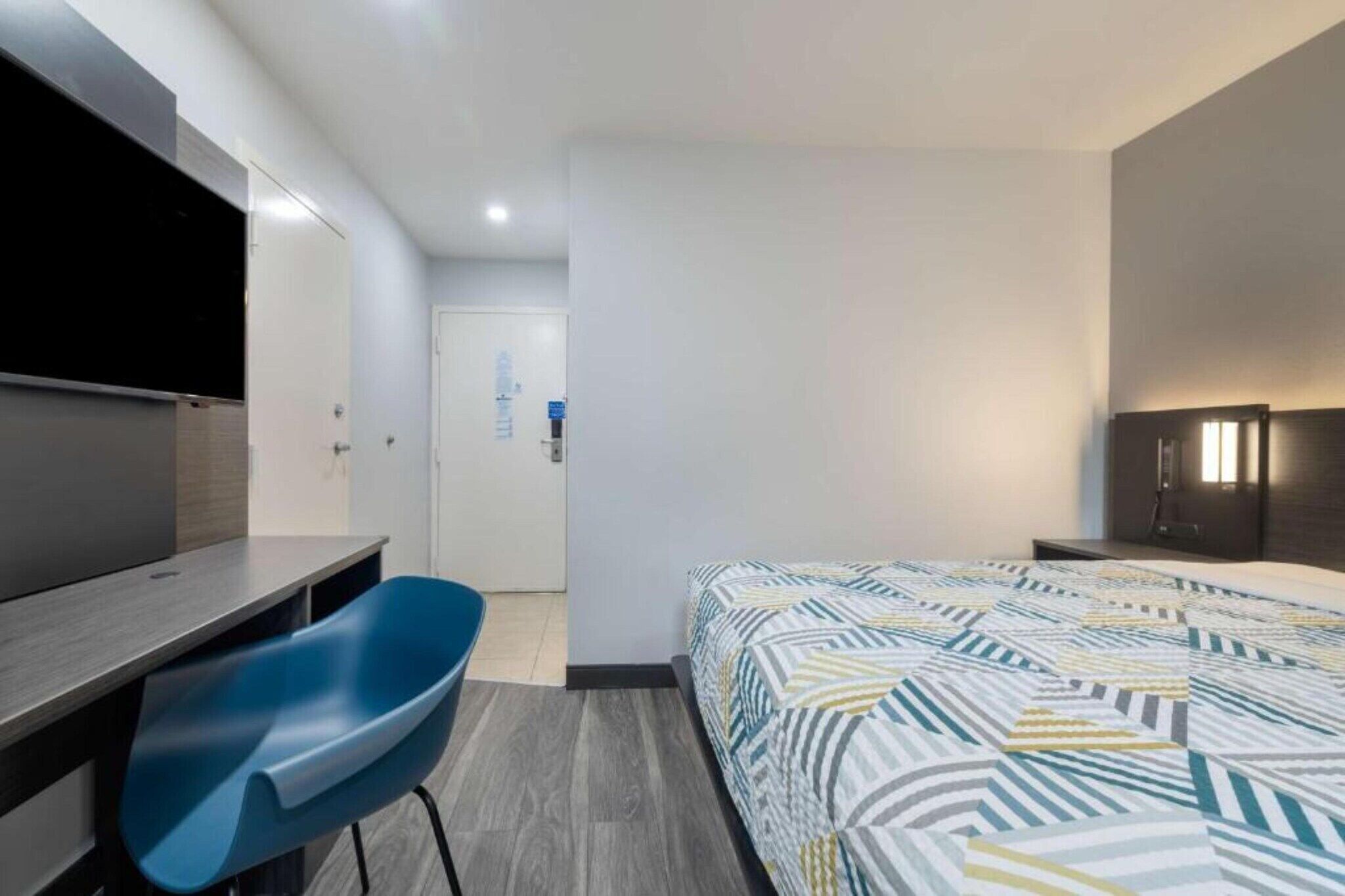 A modern hotel room with a bed, a desk, a chair, a TV, and a wardrobe.