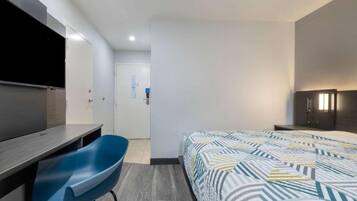 A modern hotel room with a bed, a desk, a chair, a TV, and a wardrobe.