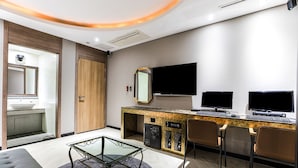 A modern hotel room with a glass coffee table, two monitors, a TV, and a bathroom with a wooden door. - Dongtan Hotel Bella (Hwaseong)
