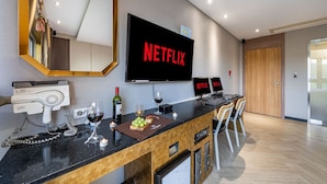 A modern hotel room with a large flat-screen TV displaying the Netflix logo, a hairdryer, a wine glass, and a bottle of wine on the counter. - Dongtan Hotel Bella (Hwaseong)
