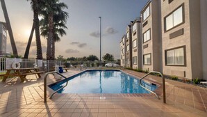 A swimming pool with tiled deck, palm trees, and a building with multiple windows. - Cozy Queen Bed|Pool|Free Parking (McAllen)