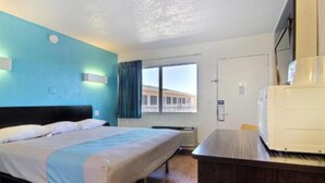 Ett hotellrum med en säng, ett skrivbord, ett fönster och en dörr.