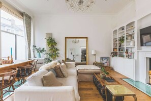 A living room with a sofa, a dining table with chairs, a fireplace, and a large mirror. - Parisian Style Duplex in Richmond Hill (Greater London)