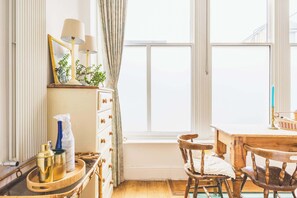 A room with a wooden table, chairs, a radiator, a window with curtains, and a mirror with lamps. - Parisian Style Duplex in Richmond Hill (Greater London)