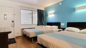 Ein Hotelzimmer mit zwei Betten, einem Schreibtisch, einem Fenster mit Vorhängen und einer blauen Wand.