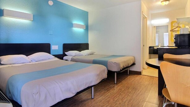 Ein Hotelzimmer mit zwei Einzelbetten, Holzboden, Schreibtisch mit Stuhl und einer kleinen Küchenzeile.
