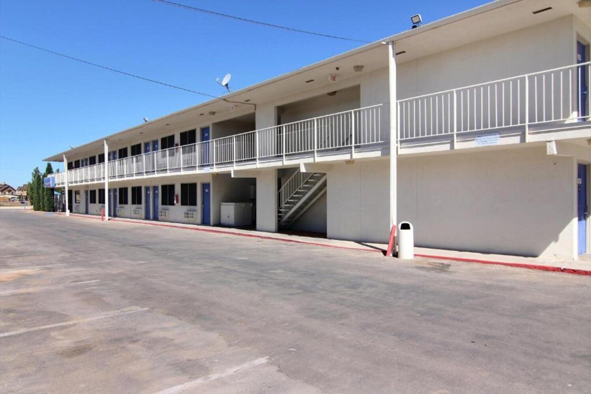 Un motel de dos pisos con una escalera central, balcones y un estacionamiento.