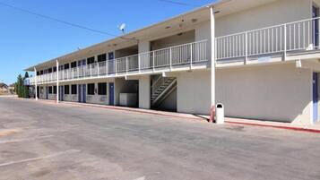 Un motel de dos pisos con una escalera central, balcones y un estacionamiento.