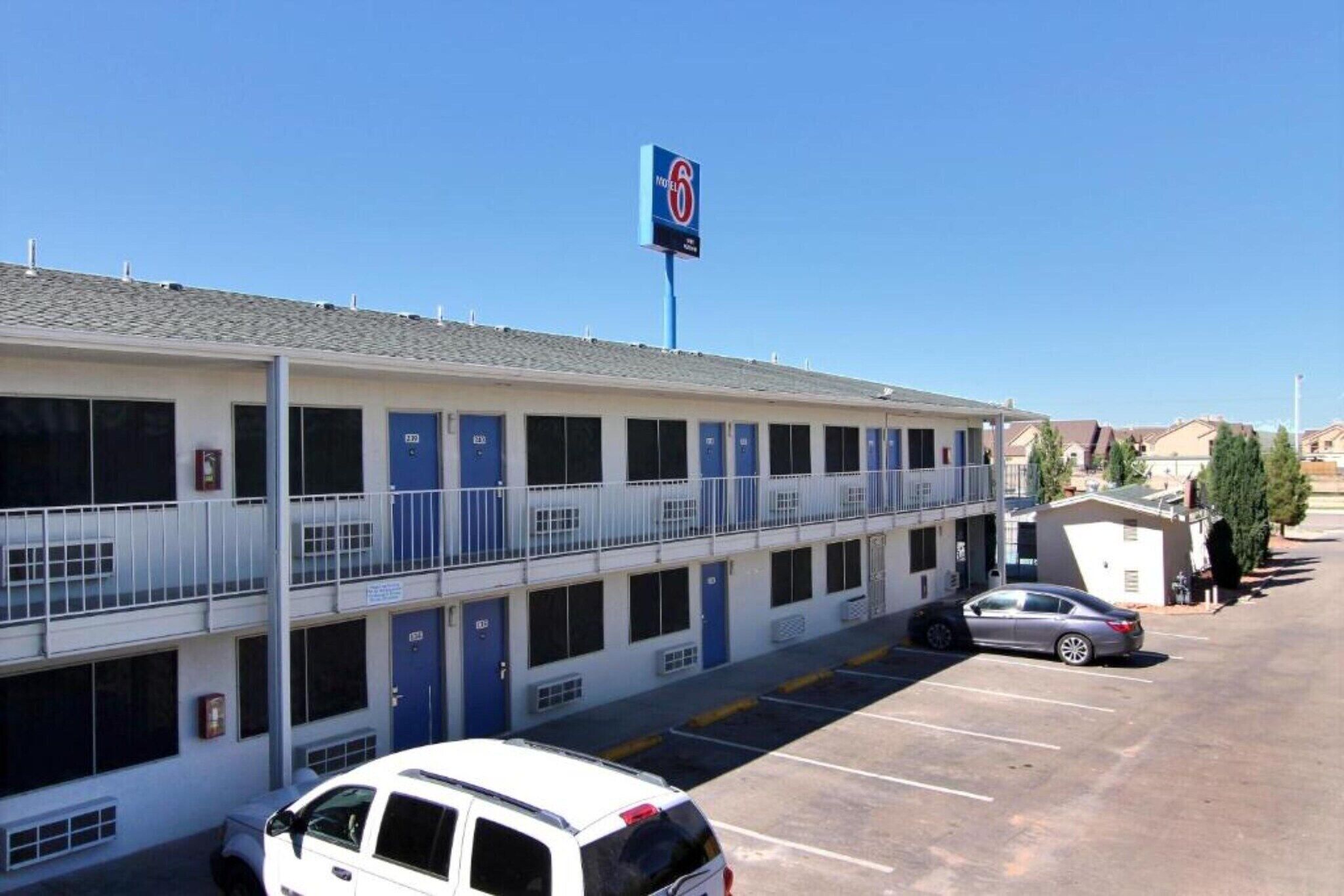 A motel with multiple rooms, a parking lot, and a clear blue sky.