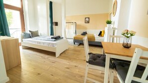 Ein modernes, helles Zimmer mit einem Bett, einem Schlafsofa, einem Esstisch und einem Stuhl.