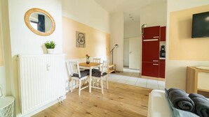 Ein modernes Wohnzimmer mit Essbereich, einer Küche im Hintergrund und einem an der Wand befestigten Fernseher.