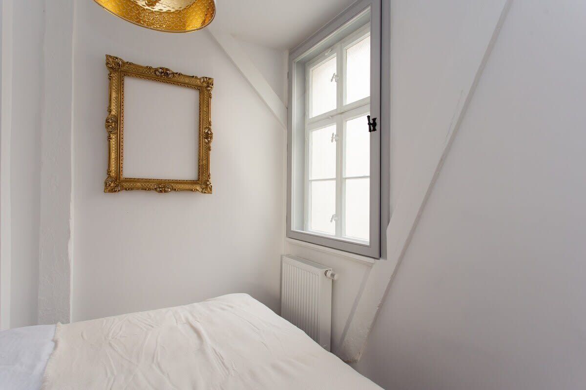 A bedroom with a white bed, a gold-framed picture frame, and a window with white shutters.