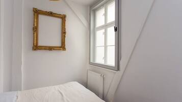 A bedroom with a white bed, a gold-framed picture frame, and a window with white shutters.