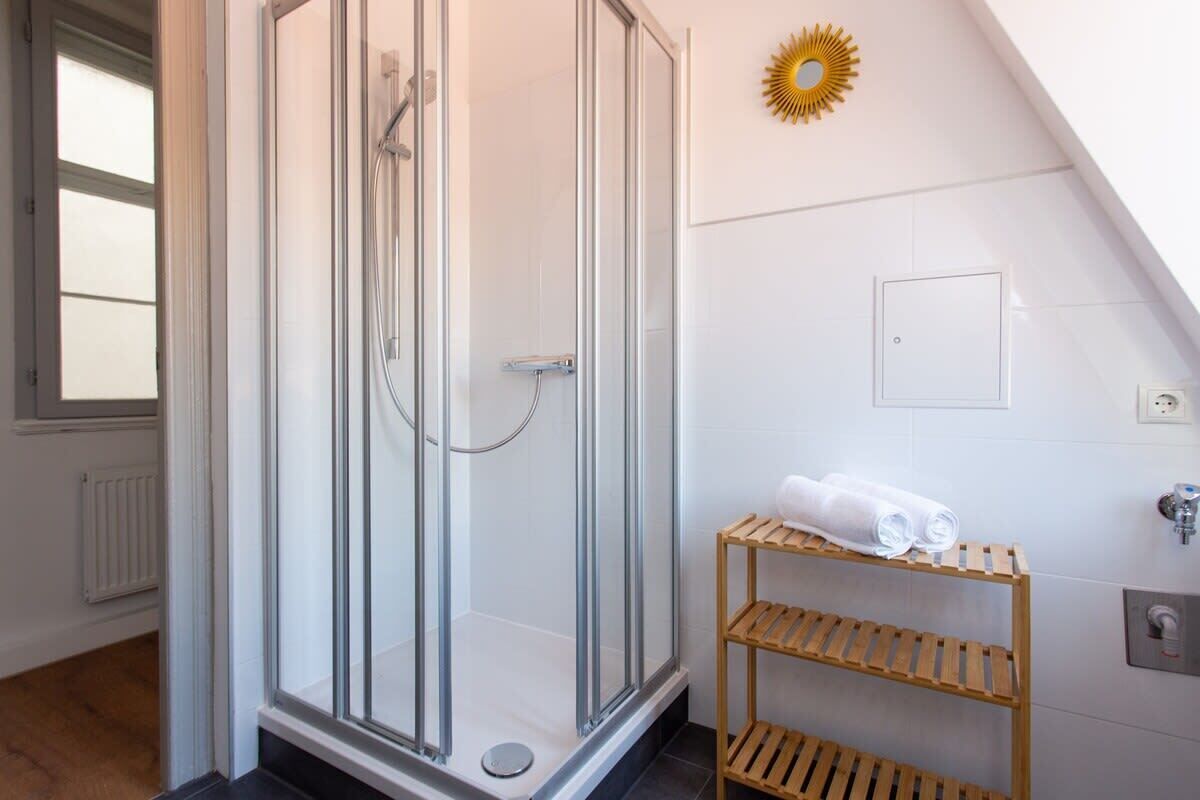 Un baño moderno con ducha de vidrio, un estante de madera con toallas y un adorno con diseño de sol en la pared.
