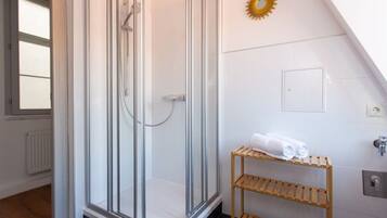 Un baño moderno con ducha de vidrio, un estante de madera con toallas y un adorno con diseño de sol en la pared.