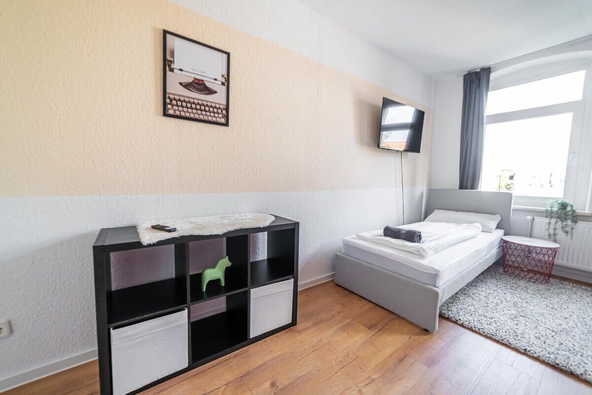 Une chambre moderne avec un lit, un meuble de rangement noir et blanc, un téléviseur fixé au mur et une fenêtre avec des rideaux.