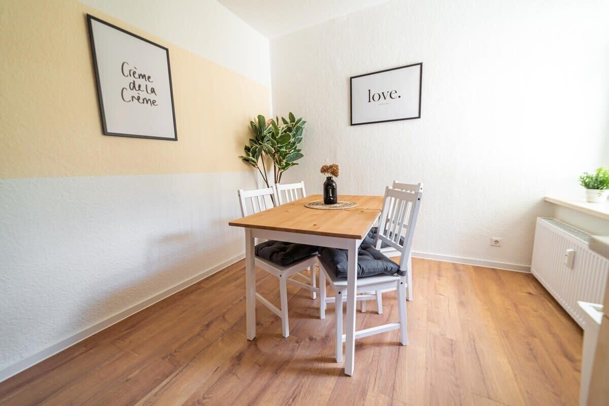 Un coin repas avec une table en bois, des chaises blanches et des œuvres d’art encadrées accrochées aux murs.