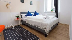 A modern bedroom with a bed, a small side table with a plant, a radiator, and a window with curtains. - FullHouse Apartments AB5 Medium (Halle (Saale))