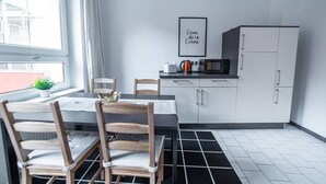 A modern kitchen with a dining table, chairs, a microwave, and a refrigerator. - FullHouse | Erfurt | M18-3 | Caribbean Dream (Erfurt)