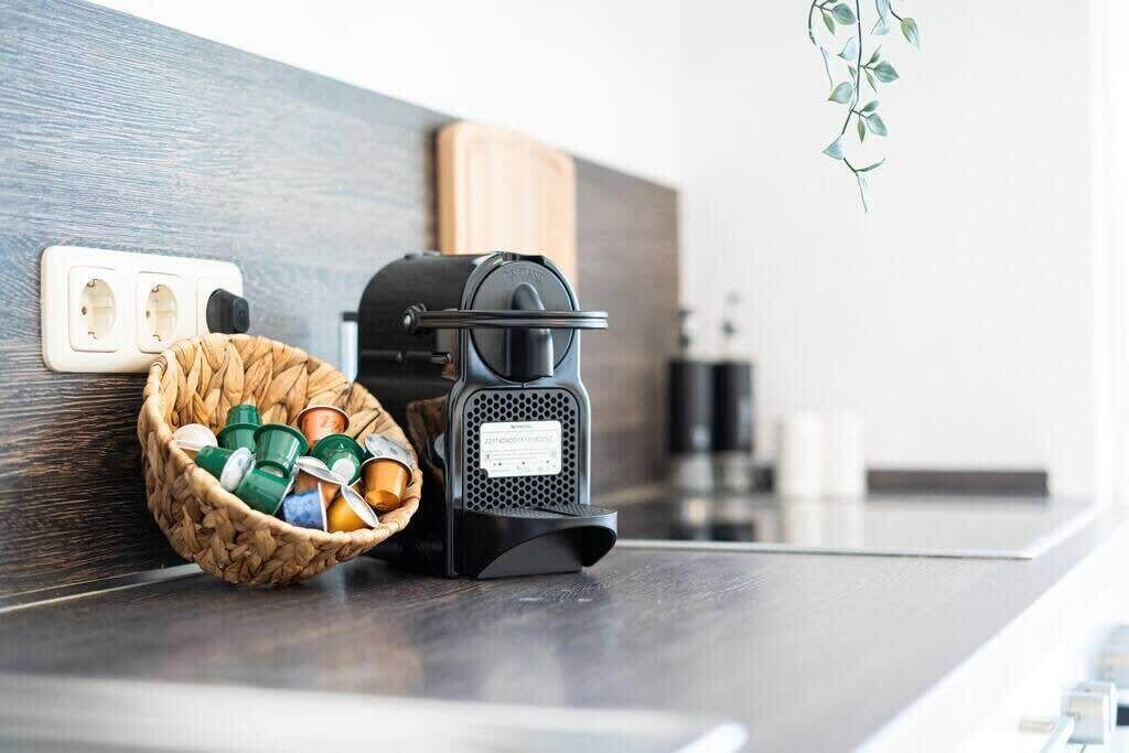 Une machine à café posée sur un plan de travail de cuisine, avec un panier de dosettes de café à proximité.