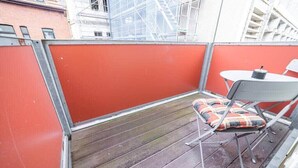 A small balcony with a red partition, a metal table with a cushion, and a chair. - FullHouse | Erfurt | M18-3 | Caribbean Dream (Erfurt)