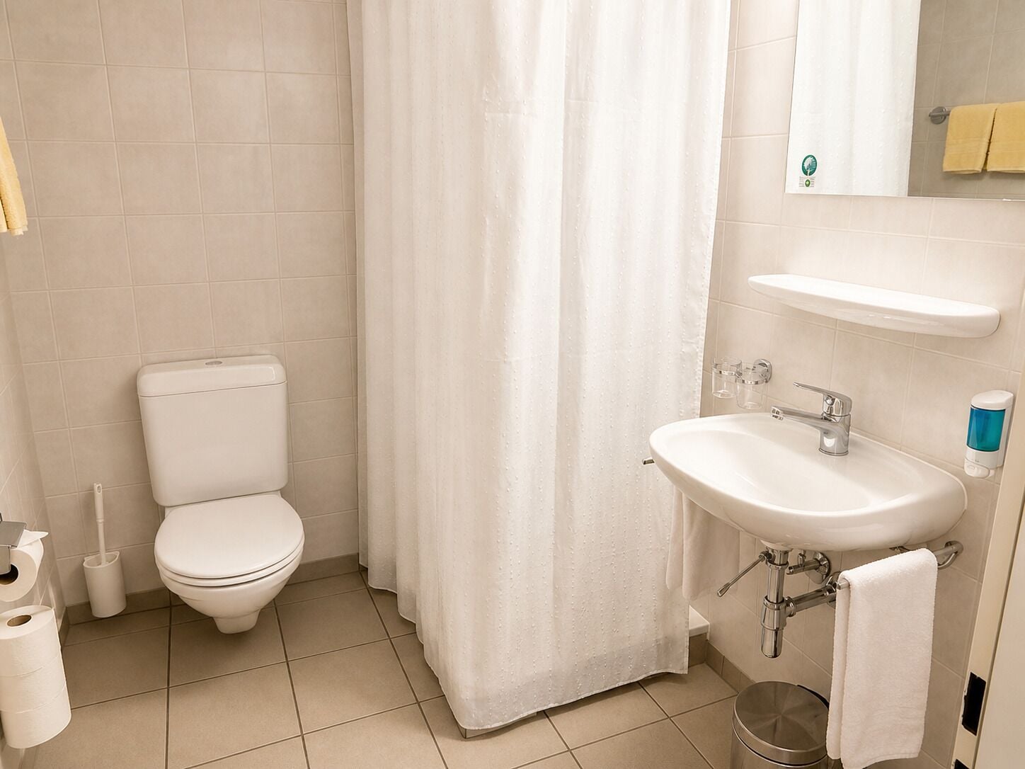 A bathroom with a toilet, a shower curtain, a sink, and a mirror.