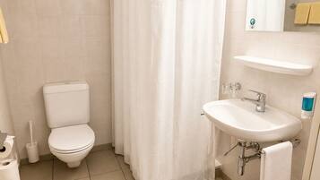 A bathroom with a toilet, a shower curtain, a sink, and a mirror.