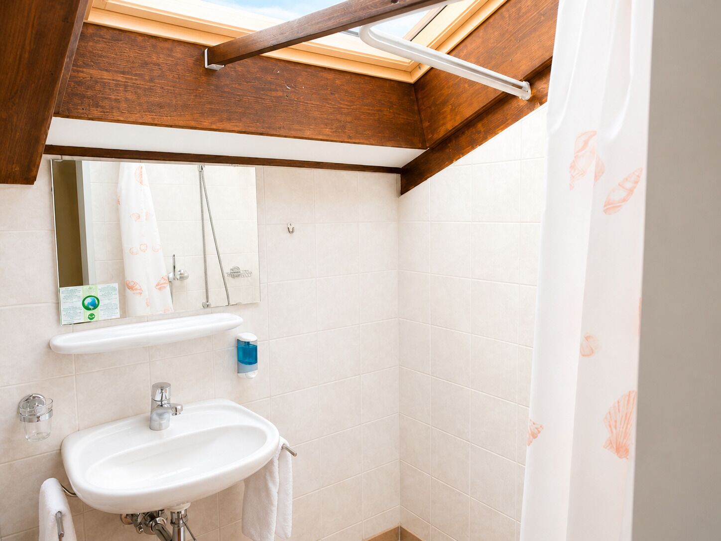 Ein Badezimmer mit Dachfenster, Waschbecken, Spiegel und Duschvorhang.