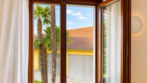 Una habitación con ventana que da a un edificio amarillo, un radiador blanco y un banco de madera.