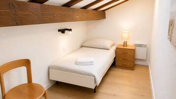 Een slaapkamer met een schuine kap, een bed, een nachtkastje, een stoel en een wandlamp.