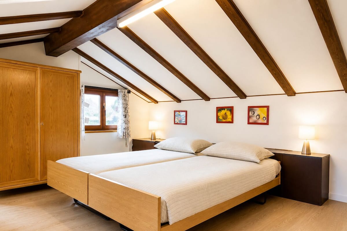 A bedroom with a wooden bed, wooden wardrobe, and a sloped ceiling with exposed beams.