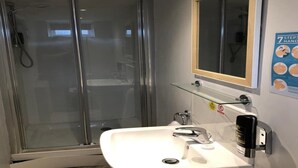 Un baño con cabina de ducha de vidrio, un lavabo blanco, un espejo y un cartel en la pared.