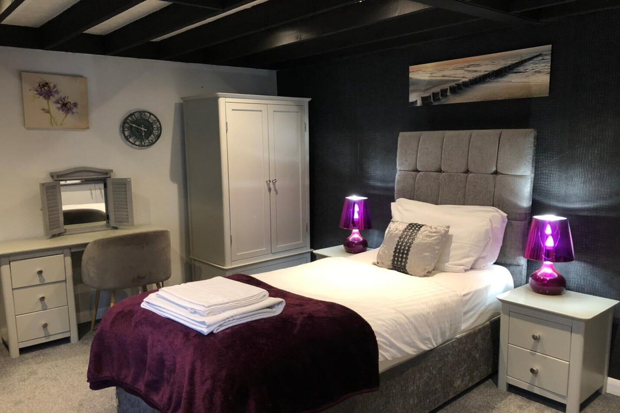 Une chambre à coucher comprenant un lit, deux lampes de chevet, une armoire, un bureau avec une chaise et une horloge murale.