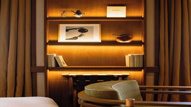 Una camera d'albergo con una libreria in legno, un quadro incorniciato e un tavolino con una sedia.
