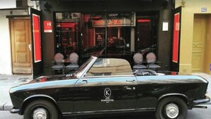 Un coche descapotable negro estacionado frente a un edificio con un letrero que dice "HOTEL".
