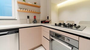 A modern kitchen with a dishwasher, oven, and a gas stove. There are wooden shelves with kitchenware and a window above the sink. - The Best in Beyoglu–Galata Tower View – Elevator – Renovated Interior – Balcony (İstanbul)