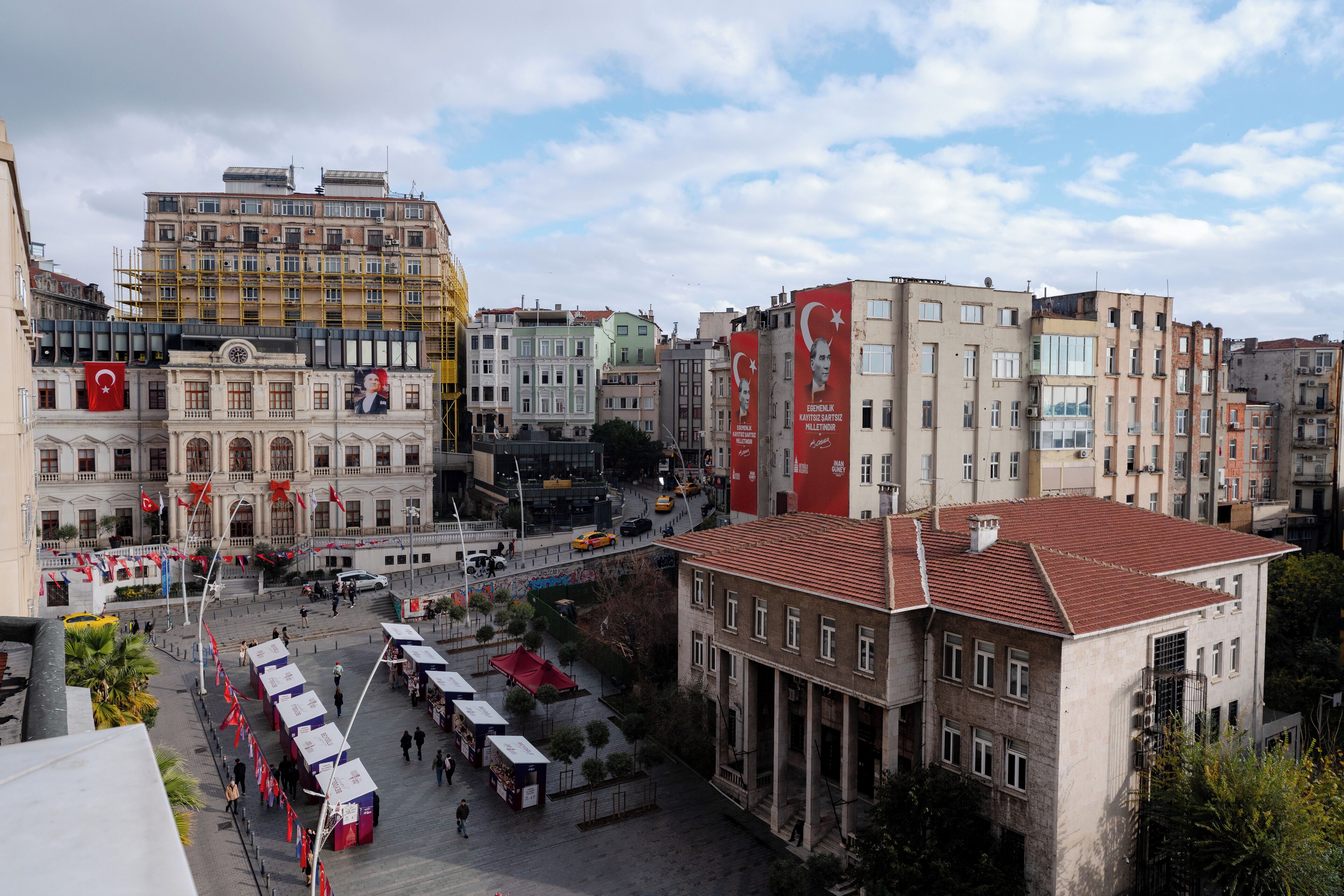 Una piazza cittadina con edifici, una torre dell'orologio e una bandiera rossa.