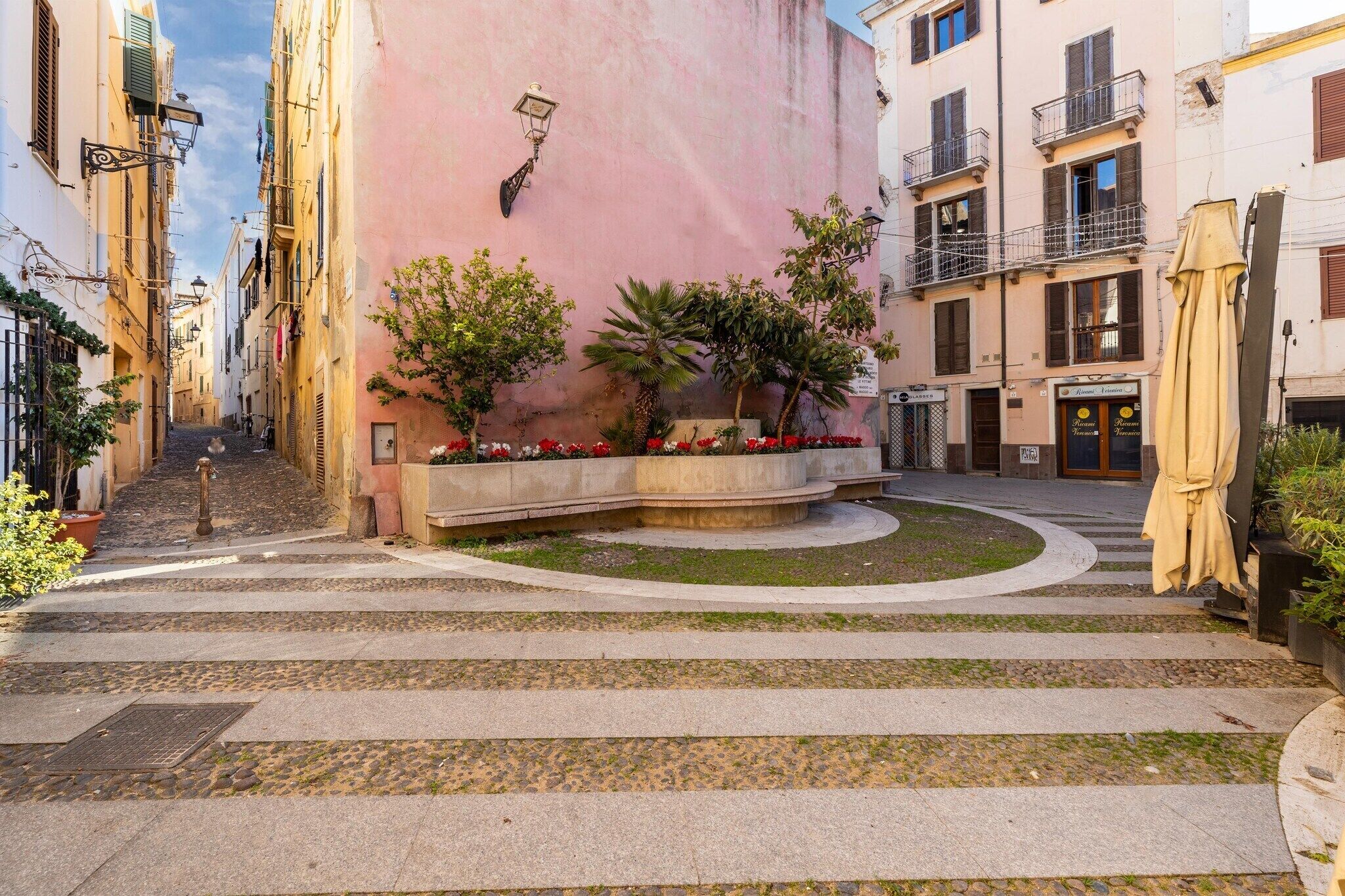 A narrow alleyway with steps leading to a building entrance, surrounded by greenery and a pink wall.