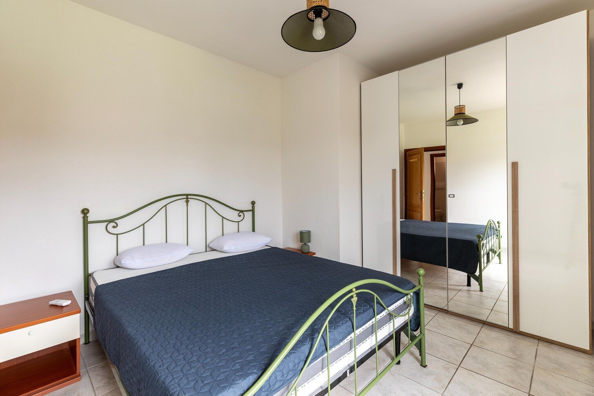 Een slaapkamer met een bed, nachtkastje, spiegel en hanglamp.