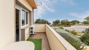 A balcony with a view of a road and trees, a window, and a small table with a green mat. - Apartment with air conditioning and terrazzo (Castelsardo)