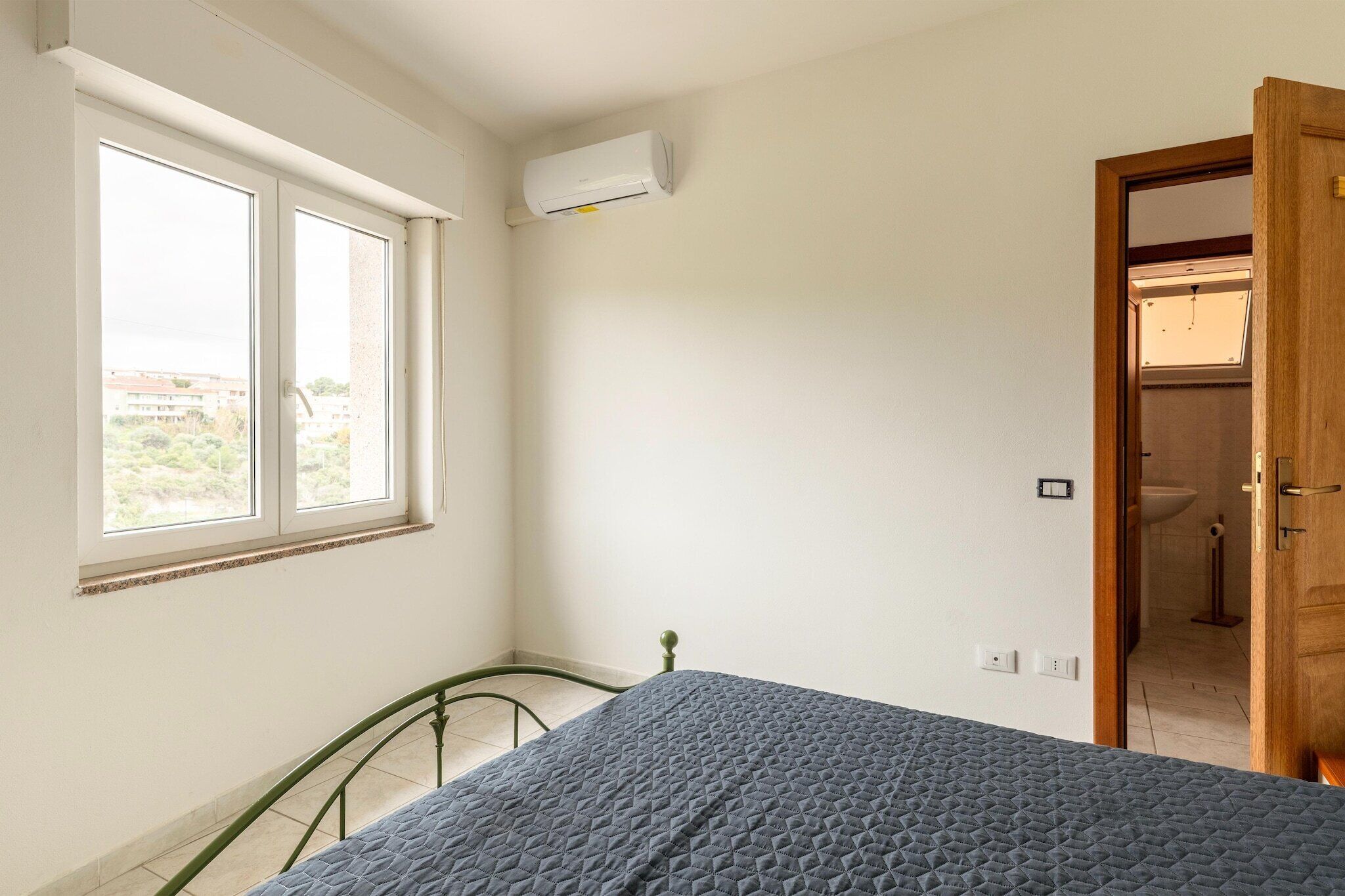 Een slaapkamer met een bed, een raam, een airconditioning en een deur naar een badkamer, plus een uitzicht op de omgeving.