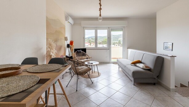 A modern living room with a dining area, a grey sofa, and a large window with a view of the outdoors. - Apartment with air conditioning and terrazzo (Castelsardo)