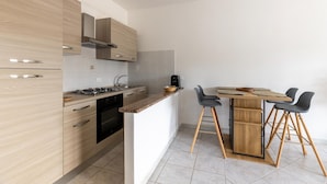 A modern kitchen with wooden cabinets, a gas stove, and a dining area with a wooden table and black chairs. - Apartment with air conditioning and terrazzo (Castelsardo)