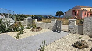 A gated entrance with a vehicle, a stone wall, and a building with a tiled roof. - A due passi dal mare, con ampio giardino (Castelsardo)