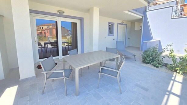A patio with a table and chairs, a sliding glass door, and a view of buildings. - A due passi dal mare, con ampio giardino (Castelsardo)
