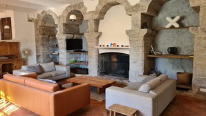 Un salon chaleureux avec des arches en pierre, une cheminée et des fauteuils confortables.