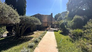 Un sentier mène à un bâtiment rustique, entouré de verdure et de grands arbres.